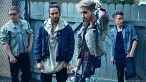 Com roupas azuis, Tokio Hotel posa para foto em frente a um muro.